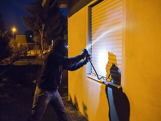 Dargestellter Einbruchversuch durch ein Fenster mit heruntergefahrenen Rollläden