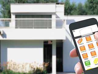 Eine in der Hand liegende Fernbedienung wird auf ein Wohnhaus gerichtet