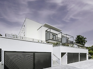 Außenansicht eines modernen Wohnhauses mit dunklen Deckenlauftoren an der Garage